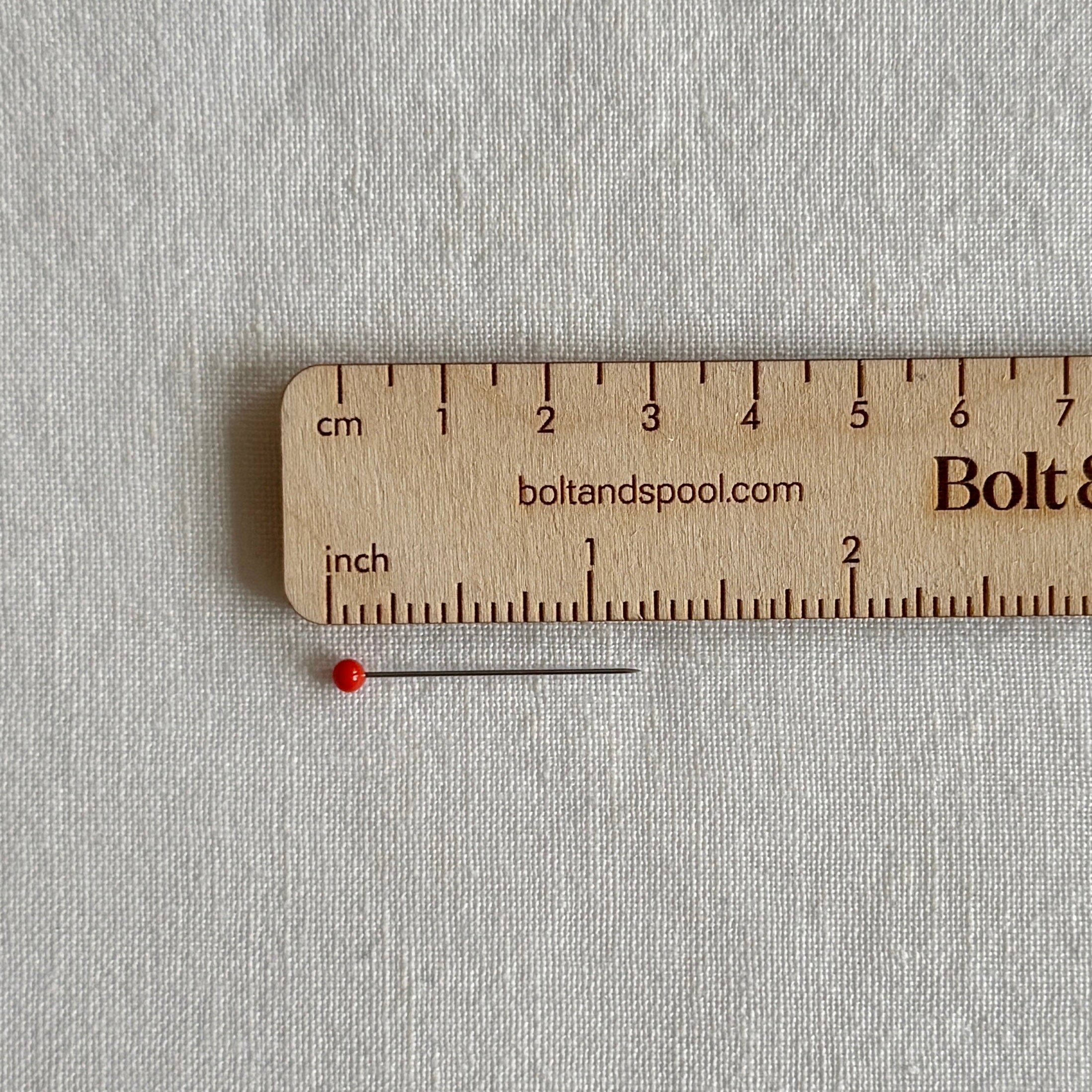 one red glass head pin next to ruler