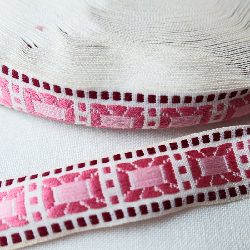 Jacquard fabric trim with pink colored rectangles & a wine colored border on white background