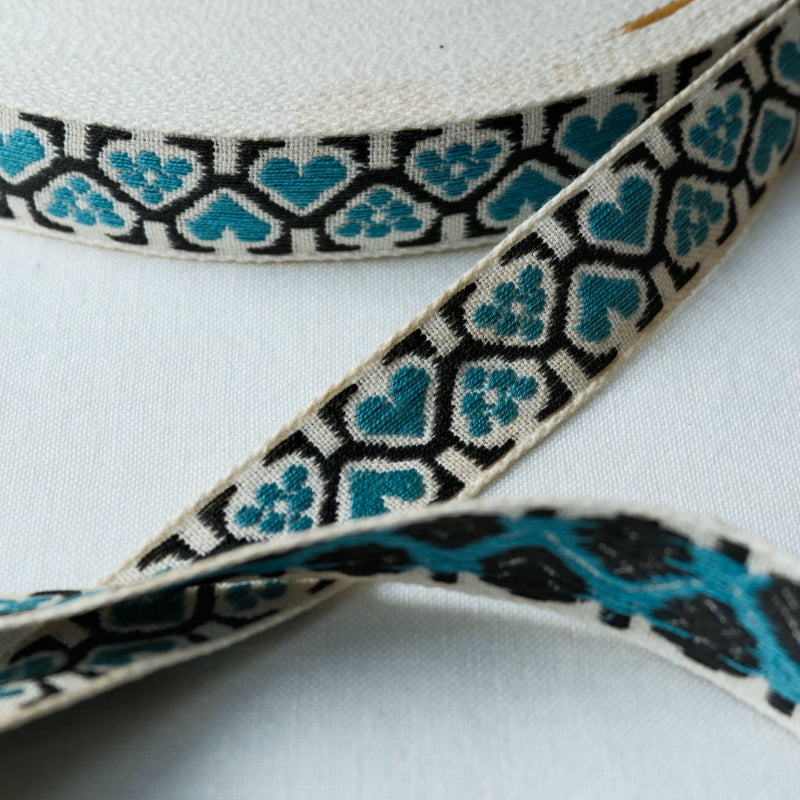 woven jacquard ribbon with teal heart pattern and black border on off white backrground
