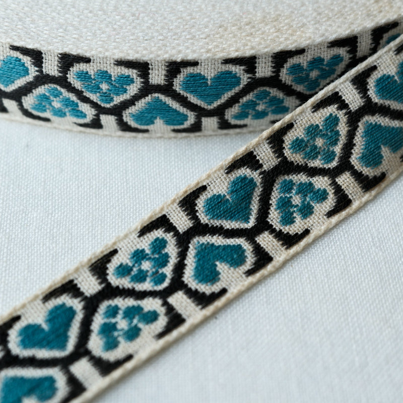 woven jacquard ribbon with teal heart pattern and black border on off white backrground